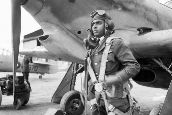 A black and white image of a man standing next to an aeroplane.